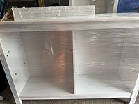 Front view of white TV stand/bookcase shrink-wrapped, two open compartments
