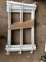 Stack of four white metal window security bar panels with mounting hooks, taped together
