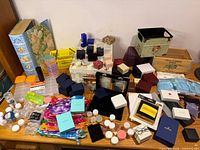 Overall view showing large quantity of cardboard jewelry boxes, plastic jars, plastic organizers, gift bags, and decorative crates on tabletop