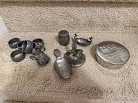 Group of pewter napkin rings, bell, scoop, condiment dishes, shaker and trinket box on carpeted step