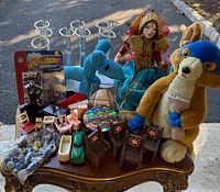 Group shot of entire lot on table showing plush toys, doll, stands, furniture, car, marbles and model kit package