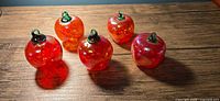 Five red glass apple ornaments on wood surface