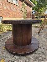 Side view of dark stained wooden cable spool showing cylindrical core and circular base