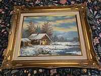 Framed oil painting of snowy cabin scene