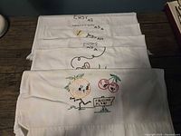 Stack of five embroidered tea towels showing top portions of designs