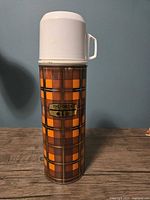 Front view of plaid Thermos showing logo, lid, stopper and full height
