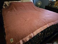 Blanket spread on queen bed showing overall color, size, satin trim and visible corner tag