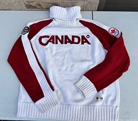 Back view of sweater displaying CANADA lettering, red sleeves, ribbed trims, Olympic patch