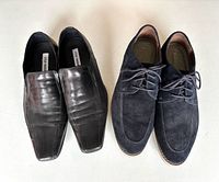 Pair of black leather loafers next to navy suede lace-ups on white surface