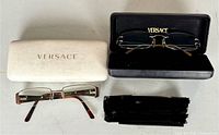 Both eyeglasses with white and black Versace cases displayed on table