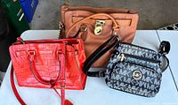 Group shot of all three Michael Kors handbags: tan tote, red satchel, black/grey logo crossbody