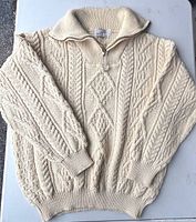Full view of cream cable knit wool sweater laid flat