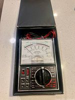 Multimeter in open black case with leads stored above meter
