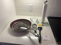 Overall view of all kitchen tools including frying pan, lid, bowls, strainer, brush and paper towel holder