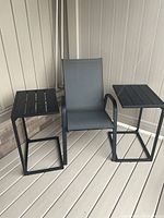 Grey sling armchair between two black C-shaped side tables on deck