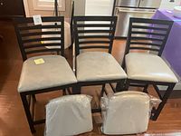 Front view of three ladder-back stools with two sealed seat cushions placed in front
