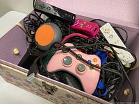 Box with pink Xbox controller, orange round device, black Wii Remote, cables