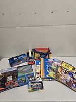 Lot overview showing boxed TrackMaster train, carry bag, Busy Book, die-cast engine and stack of hardcover books