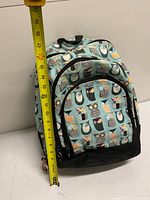 Front view of owl print backpack with tape measure showing height around 18 inches