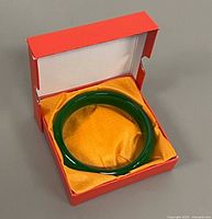Jade bangle positioned inside open red box with yellow satin lining