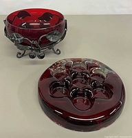 Bowl in wrought iron stand alongside red glass disk