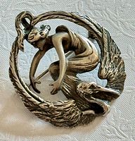 Front view of sterling brooch-pendant showing female figure, bird and feather wreath design