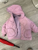Pink quilted jacket and red umbrella on floor