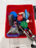 Red bin containing kettlebell, medicine balls, yoga blocks, weighted bar handles