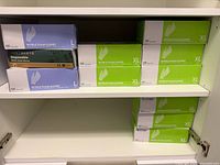 Cabinet shelves with ten boxes of nitrile exam gloves, showing sizes and packaging