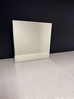 Single square mirror tile leaning against dark wall