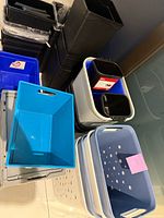 Stacked assortment showing tall black bins, blue recycling boxes, ventilated baskets and totes