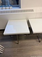 Two square white side tables with metal legs placed side by side