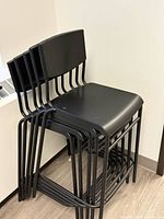 Five black bar-height chairs stacked, showing side profile and footrests