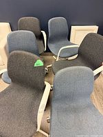 Six mixed blue and charcoal upholstered office chairs with white metal armrests and caster bases