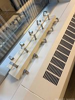 White metal rail coat rack with eight chrome L-shaped hooks