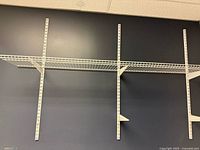 Wall-mounted wire shelf installed on four vertical standards with support brackets