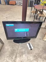 Front view of Samsung TV on stand with screen powered on, remote and manual visible