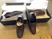 Both pairs of Alfani brown dress shoes in their boxes with tissue, oxford on left, loafer on right