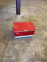 Front view of red metal cooler with cream base, showing chrome latch and Coleman logo