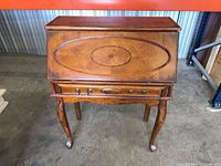 Front view closed showing inlaid panel, brass pulls, cabriole legs, overall finish