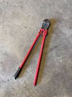 Full view of bolt cutter showing red handles, black head, one rubber grip