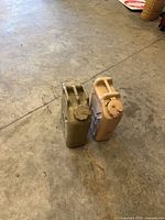 Two jerry cans on floor; tan water can at right with desert sand color and screw cap