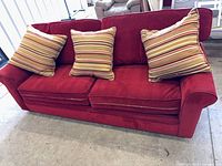 Front view of red corduroy sofa with three striped pillows