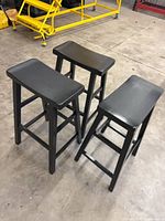 three black wooden bar-height stools grouped together