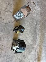 All three items laid out: tall lantern with ring handle, small geometric lantern, wall fixture cover