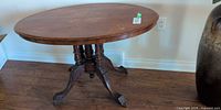 Full view of antique oval pedestal table showing carved pedestal base and casters
