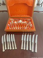 Open wooden box displaying silver-plated flatware pieces in orange lining
