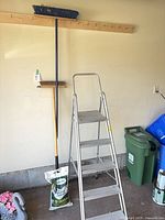 ladder folded out beside push broom; shows overall condition and size