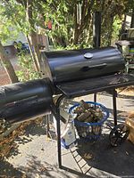 Full view of smoker on cart with basket of logs beneath