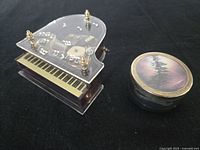 Grand piano shaped music box and round photo frame music box side by side